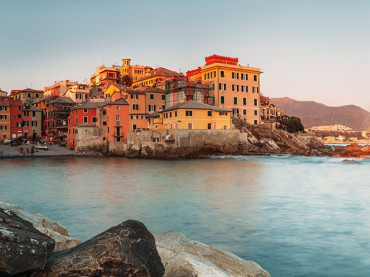 Malerisches Boccadasse, Genua: Bunte Häuser am Strand, ruhiges Meer und Berge bei Sonnenuntergang.