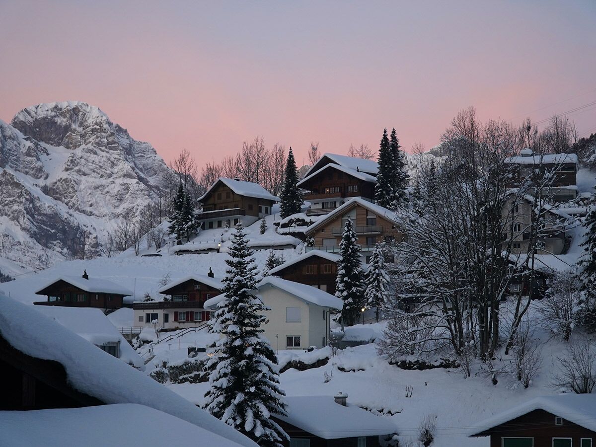 Malerisches Bergdorf in den Alpen, tief verschneit unter einem rosafarbenen Abendhimmel bei Sonnenuntergang.