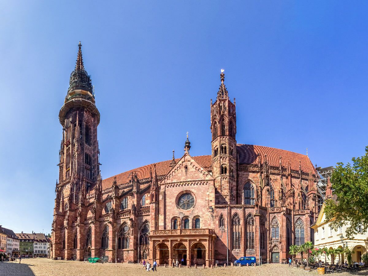 Freiburger Münster, gotische Kathedrale aus rotem Sandstein am sonnigen Marktplatz in Freiburg im Breisgau, Deutschland. Besucher und Cafés.