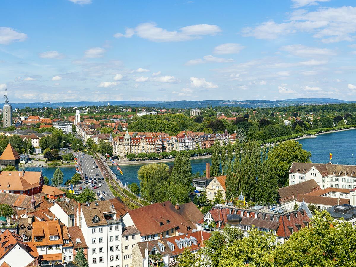 Panoramablick auf Konstanz am Bodensee mit Rheinbrücke, Altstadt und grünen Ufern unter blauem Himmel an einem Sommertag.