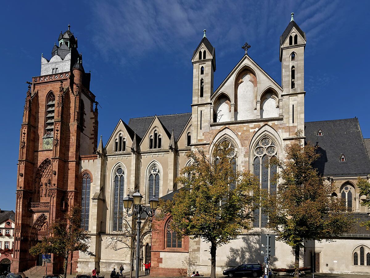 Historische Kirche mit rotem Backsteinturm und gotischen Elementen im Herbstlicht unter blauem Himmel mit Bäumen.