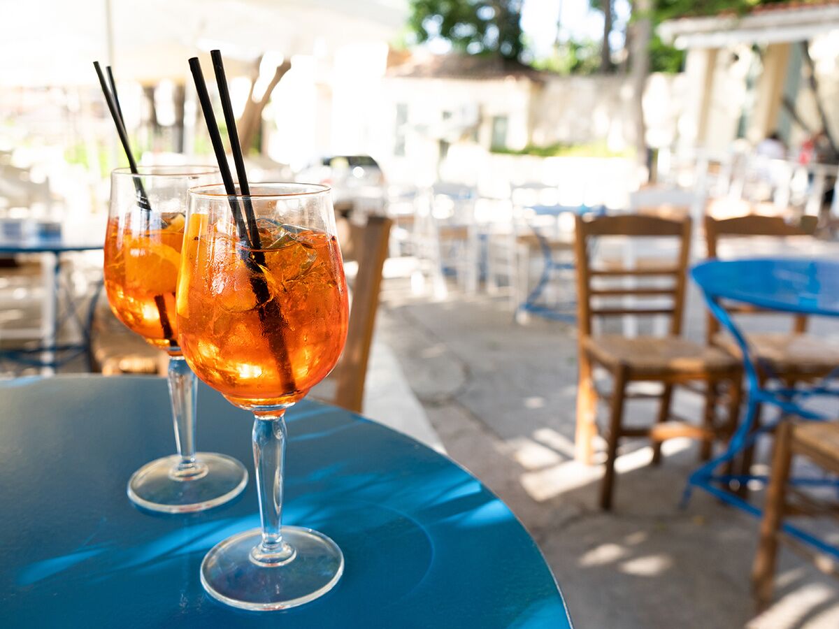 Zwei erfrischende Aperol Spritz mit Orangen und Strohhalmen auf einem blauen Terrassentisch in einem sonnigen Café.