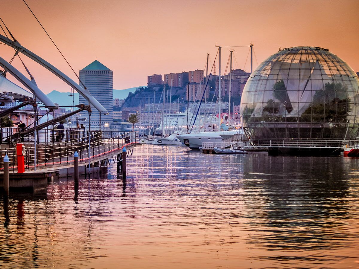 Panoramaansicht des Alten Hafens von Genua mit dem Il Bigo, der Biosfera und Booten im warmen Abendlicht.