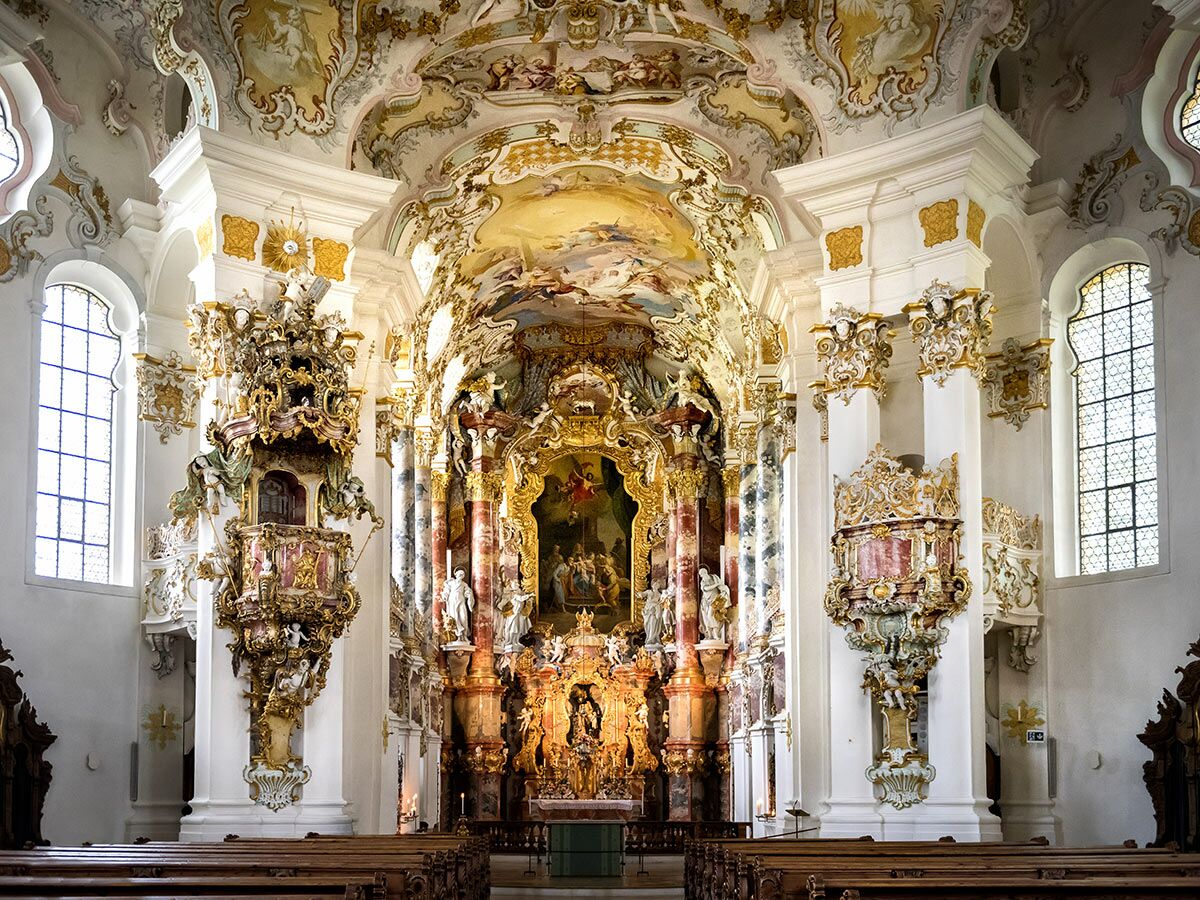 Opulente Innenansicht einer Rococo-Kirche mit reich verziertem Hochaltar, Fresken, Kanzel, Stuck und goldenen Details.