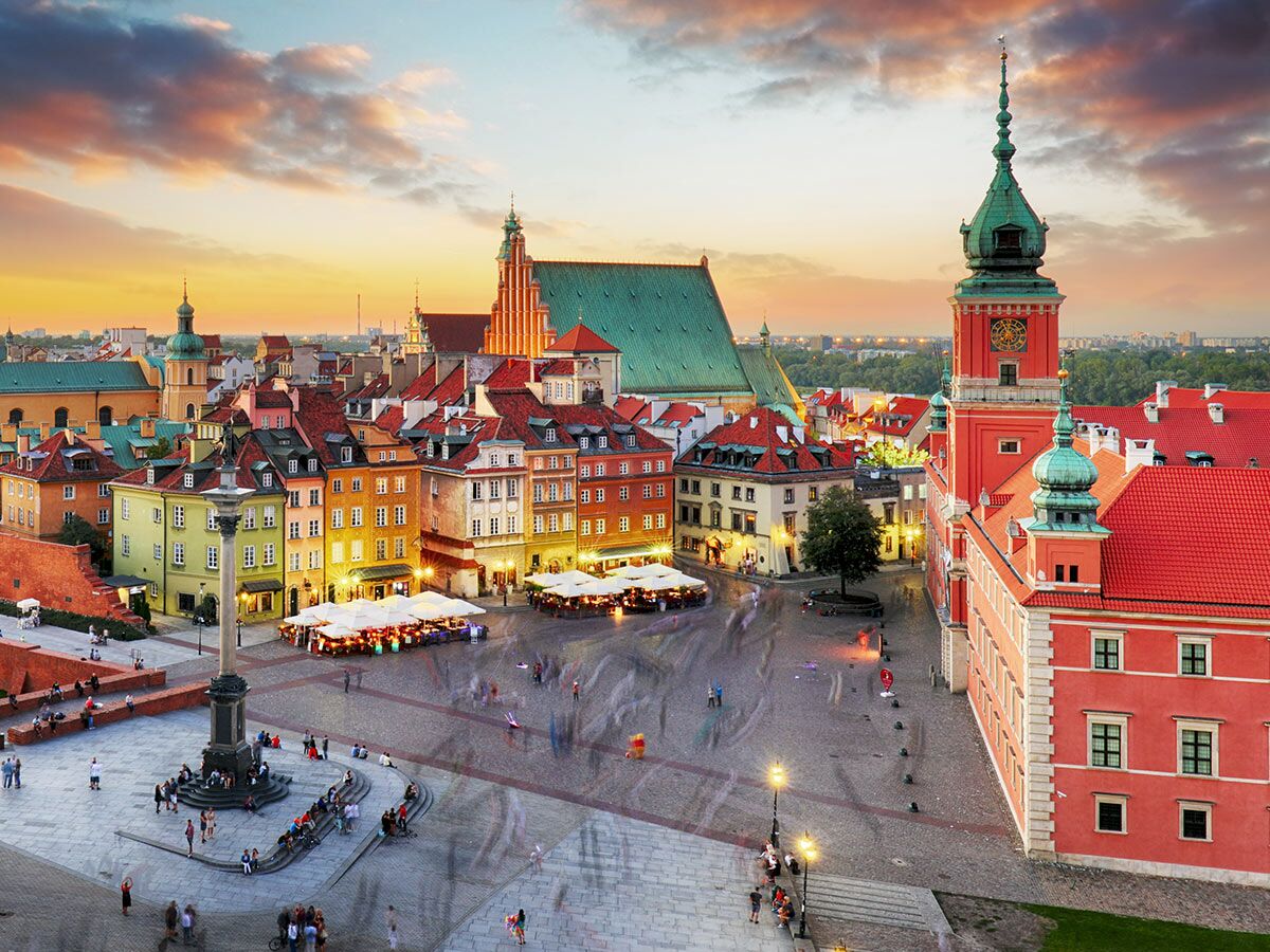 Blick auf Warschaus Altstadt bei Sonnenuntergang mit farbenfrohen Gebäuden, dem Schlossplatz, der Sigismundsäule und dem Königsschloss.
