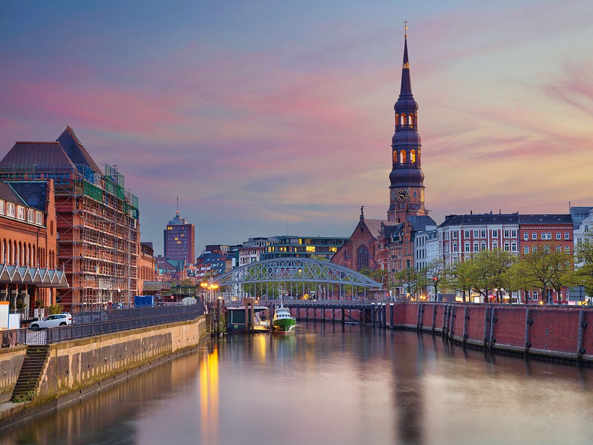 Abenddämmerung in Hamburg: Nikolaifleet mit beleuchteter St. Katharinen Kirche, historischen Backsteingebäuden und Wasserreflexionen.
