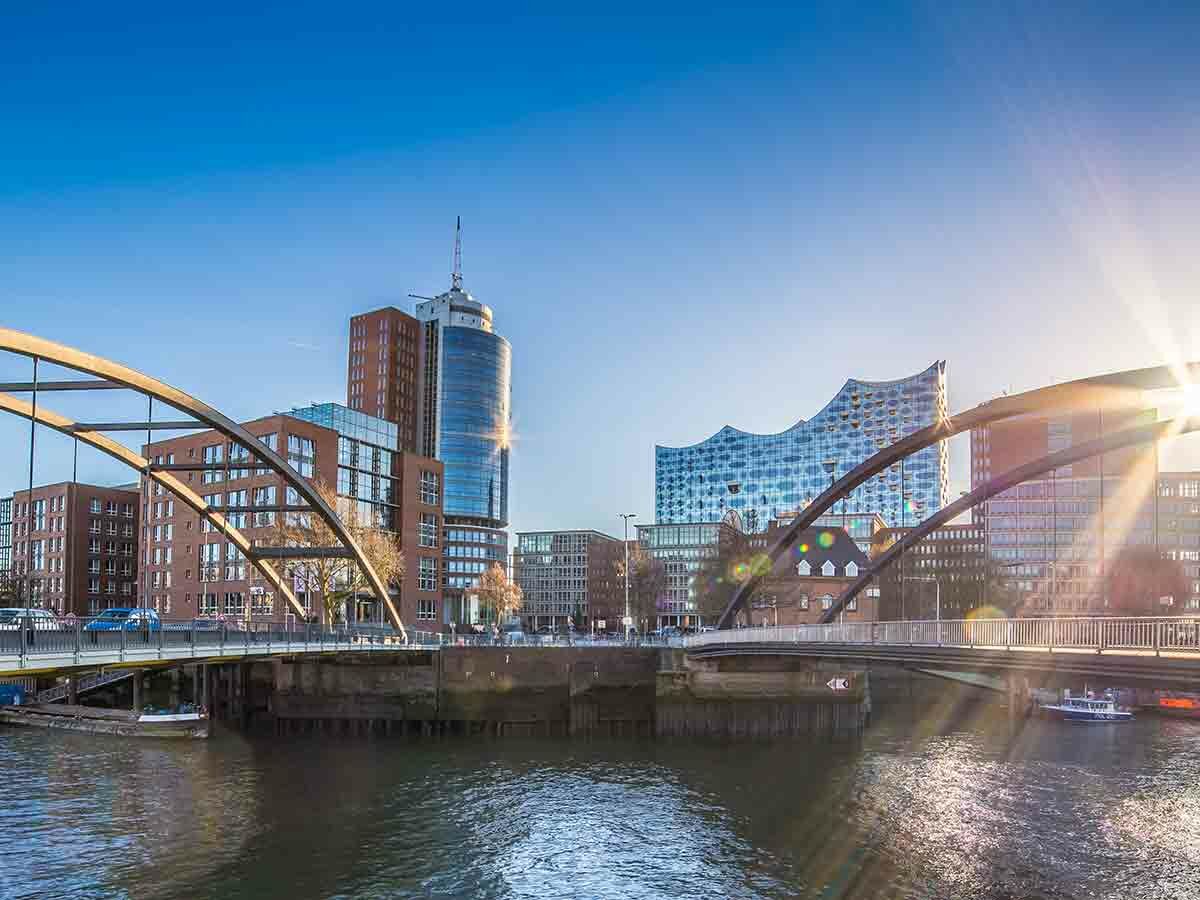 Skyline von Hamburg HafenCity mit Elbphilharmonie, modernen Gebäuden, Brücken und Wasser bei Sonnenschein.