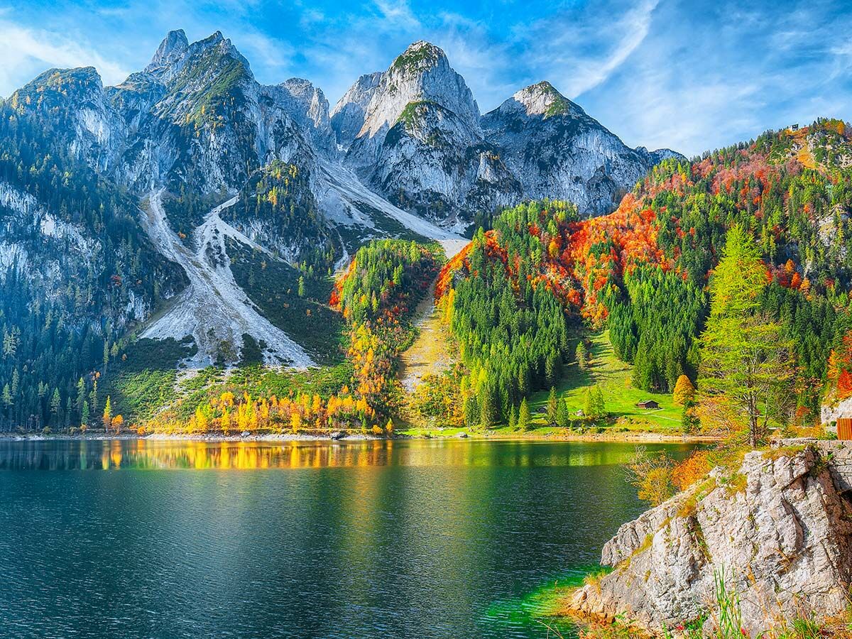 Majestätischer Gosausee mit spiegelnden Berggipfeln und farbenprächtigem Herbstwald unter blauem Himmel.
