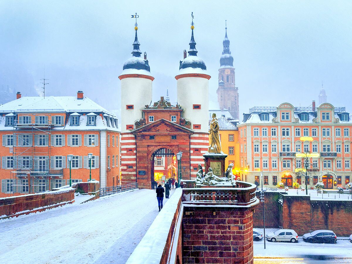 Winterlicher Blick auf Heidelbergs Alte Brücke, das Brückentor und verschneite Altstadt. Abends, Menschen gehen über die Brücke.