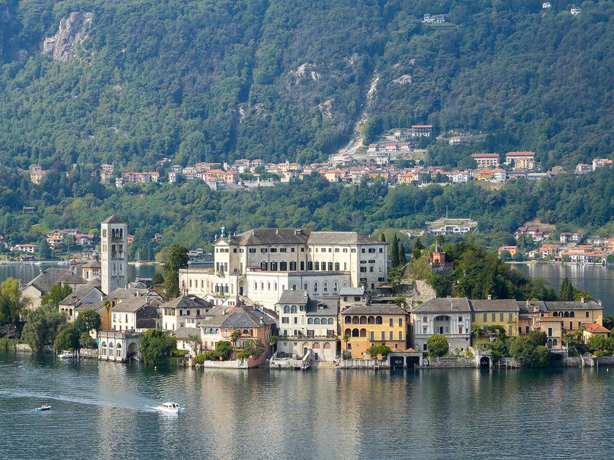 Panoramablick auf die Isola San Giulio im Ortasee mit historischen Gebäuden, Kirchturm und grünen Hügeln. Boote auf dem Wasser.