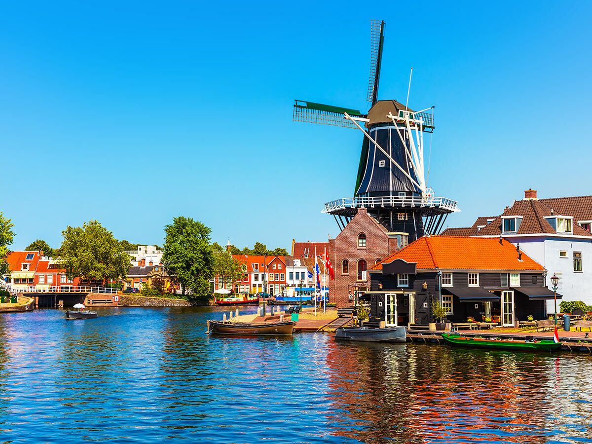 Blick auf die historische Windmühle De Adriaan in Haarlem, Niederlande, mit Gracht, Booten und traditionellen Häusern.