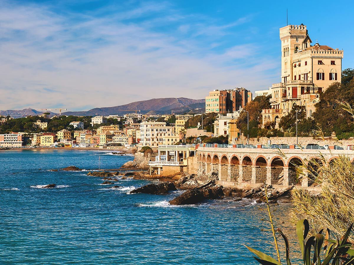 Malerische Küstenstadt Genua, Italien mit bunten Häusern, blauem Meer, Schloss und Küstenpromenade.
