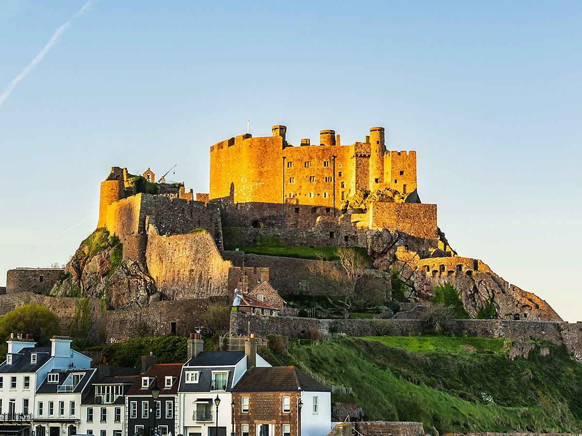 Historisches Mont Orgueil Schloss in Jersey, beleuchtet von der warmen Abendsonne, mit Häusern am Fuße des Hügels.