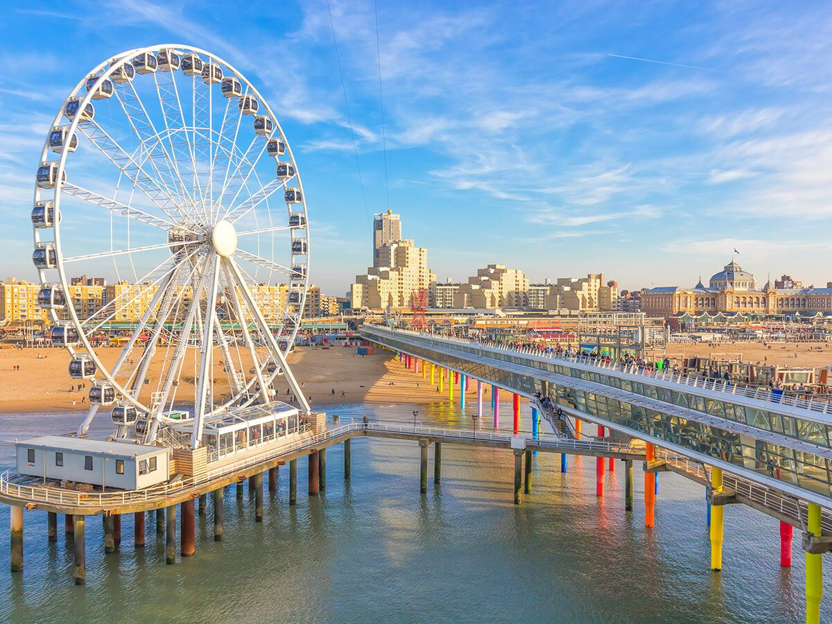 Großes Riesenrad auf einer modernen Seebrücke am Strand von Scheveningen mit Stadtpanorama und blauem Himmel.