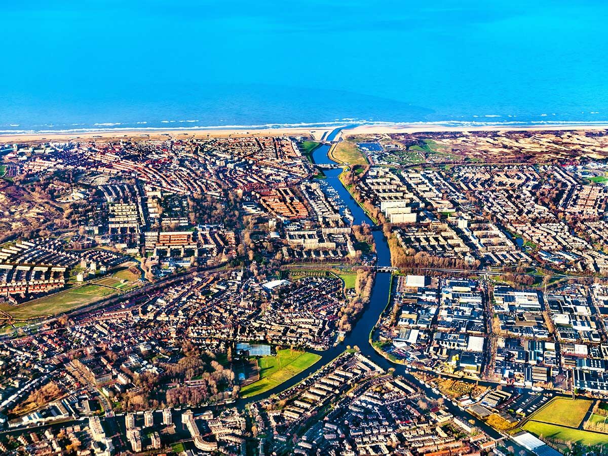 Luftaufnahme einer Küstenstadt mit Wohnhäusern, einem Fluss, der ins Meer mündet, Sandstrand und weitem Ozean.