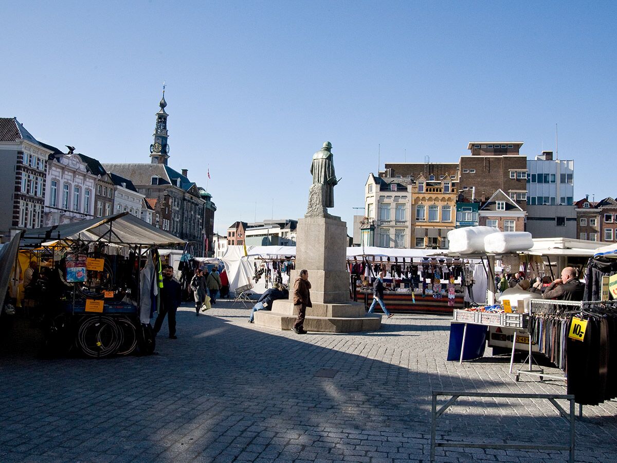 Menschen bummeln an Marktständen auf einem Kopfsteinpflasterplatz mit historischer Architektur, Glockenturm und Statue.