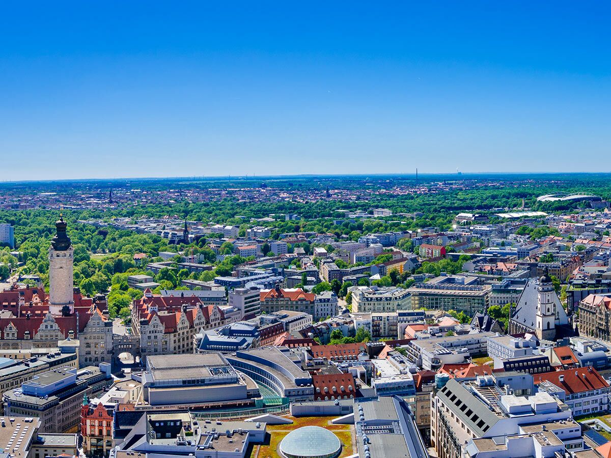 Luftaufnahme von Leipzig mit Neuem Rathaus, Thomaskirche und Red Bull Arena unter blauem Himmel.