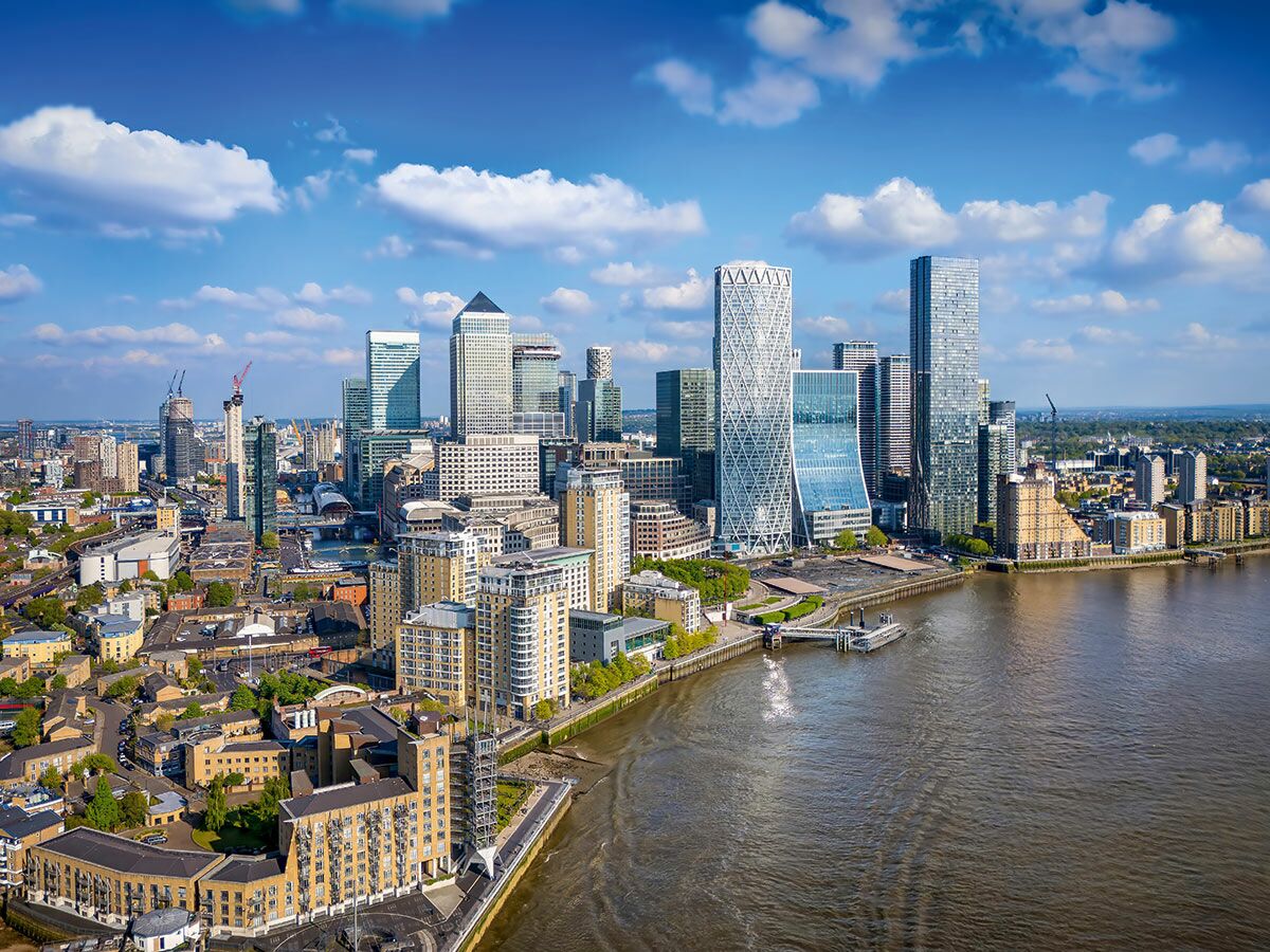 Panorama von Londons Canary Wharf mit modernen Wolkenkratzern und der Themse unter blauem Himmel.