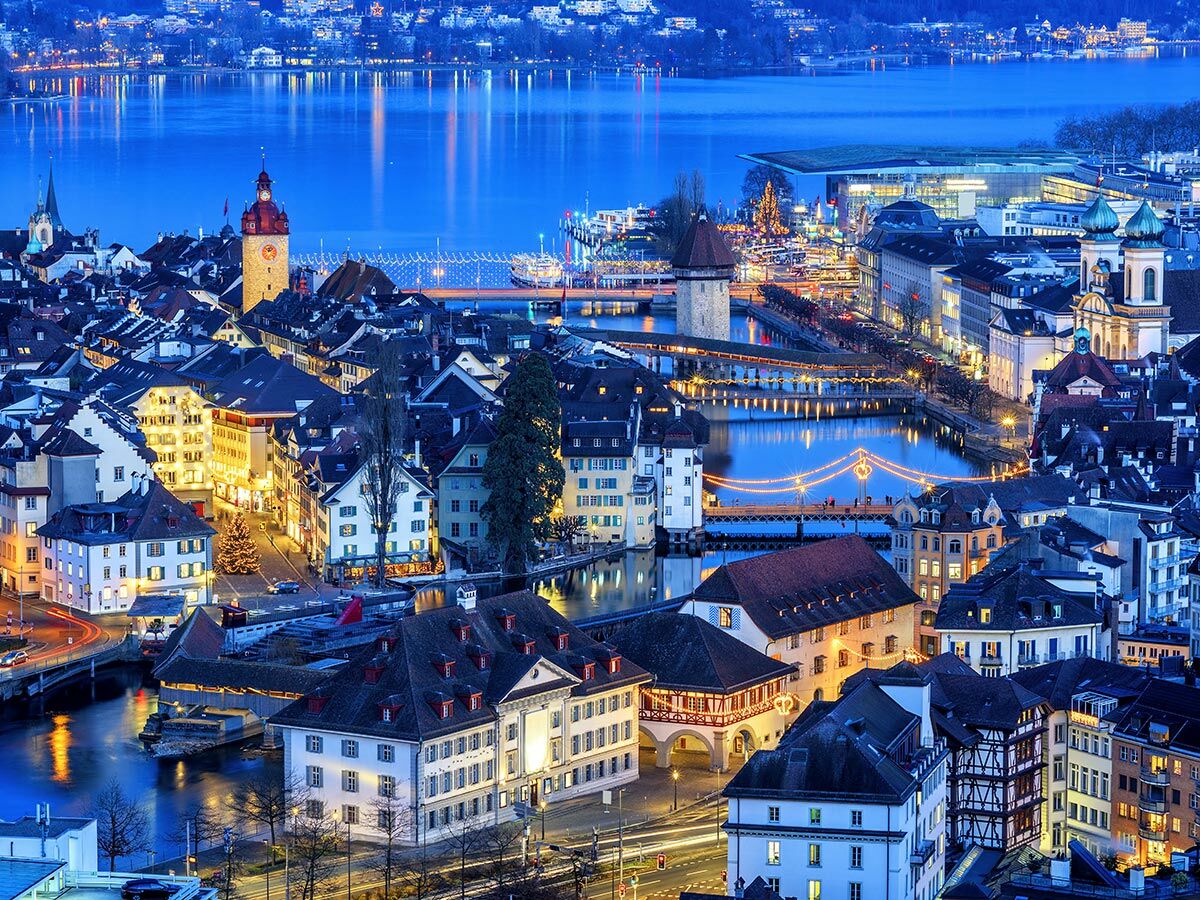 Panoramablick auf die beleuchtete Luzerner Altstadt bei Nacht, mit Kapellbrücke, Reuss und Vierwaldstättersee im Hintergrund.