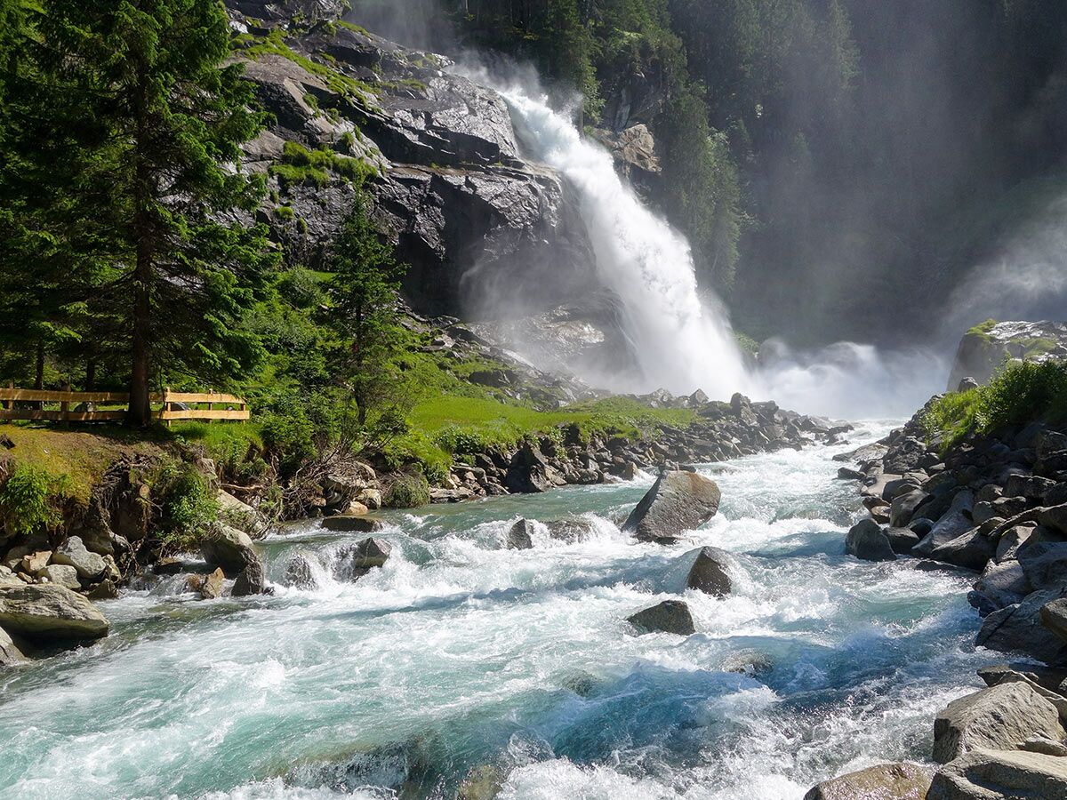 Majestätischer Wasserfall in den Alpen, klares Wasser eines rauschenden Gebirgsflusses fließt durch grüne Wälder und Felsen.