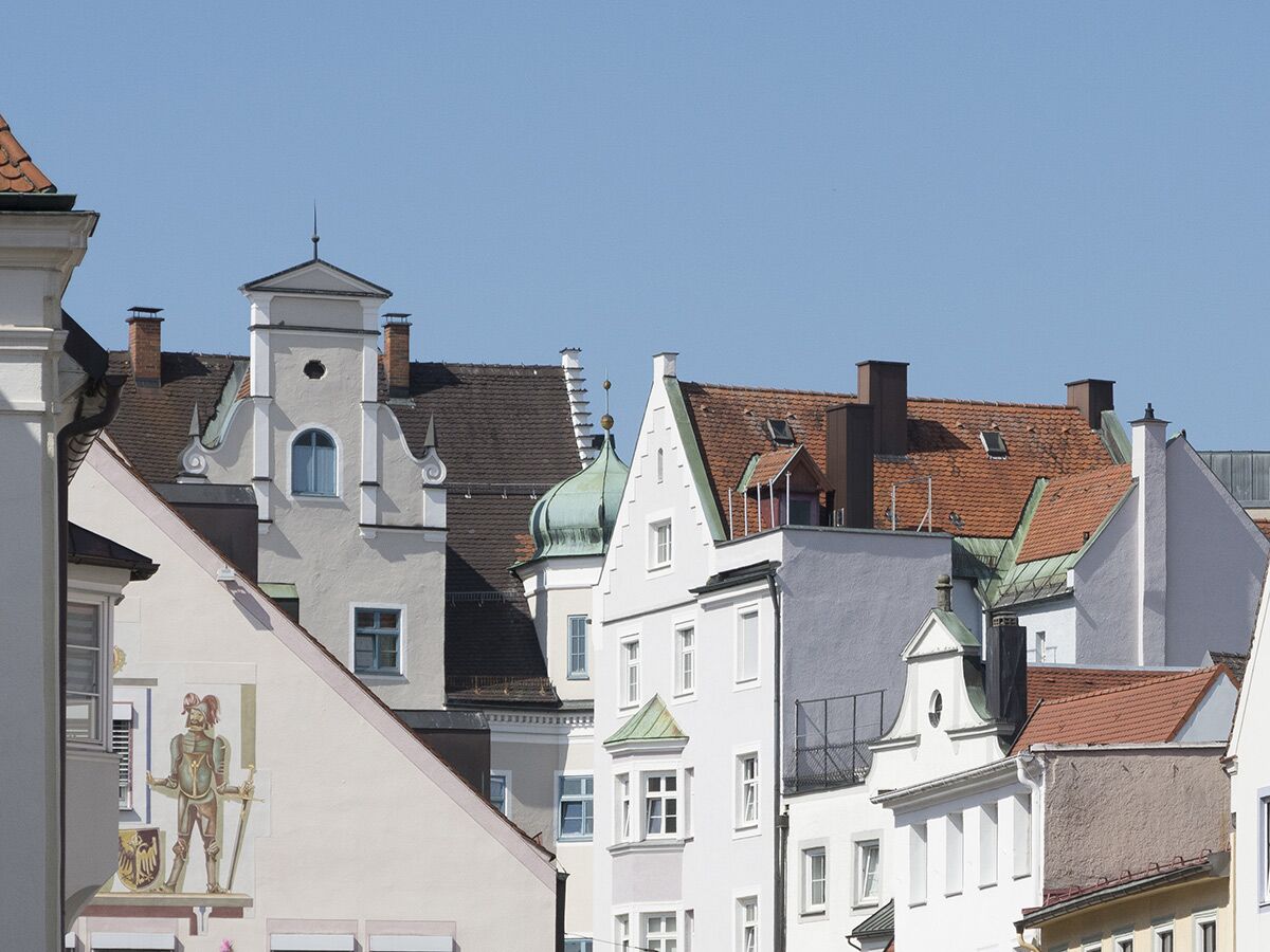 Nahaufnahme historischer Häuserfassaden und Dächer mit Giebeln, Schornsteinen und blauen Himmeln in einer europäischen Altstadt.