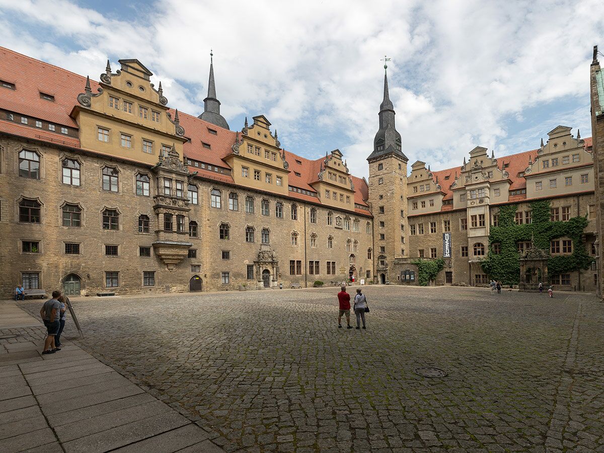 Blick auf den weitläufigen Innenhof des historischen Schlosses Coburg mit steinernen Gebäuden, Türmen und Giebeln unter bewölktem Himmel.