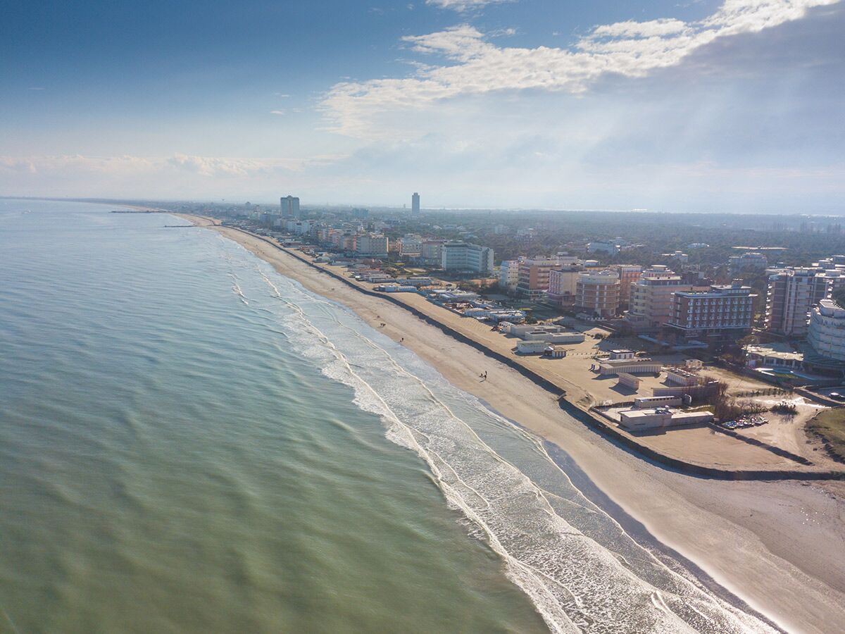 Luftaufnahme des langen Sandstrandes mit Wellen und Küstenstadt mit Hotels und Gebäuden unter blauem Himmel.