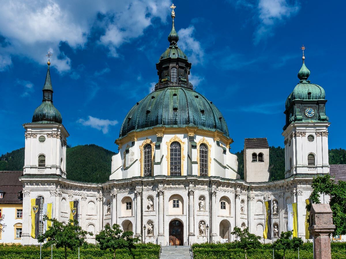 Majestätisches Kloster Ettal in Bayern mit barocker Architektur, grünen Kuppeln und Türmen unter blauem Himmel.