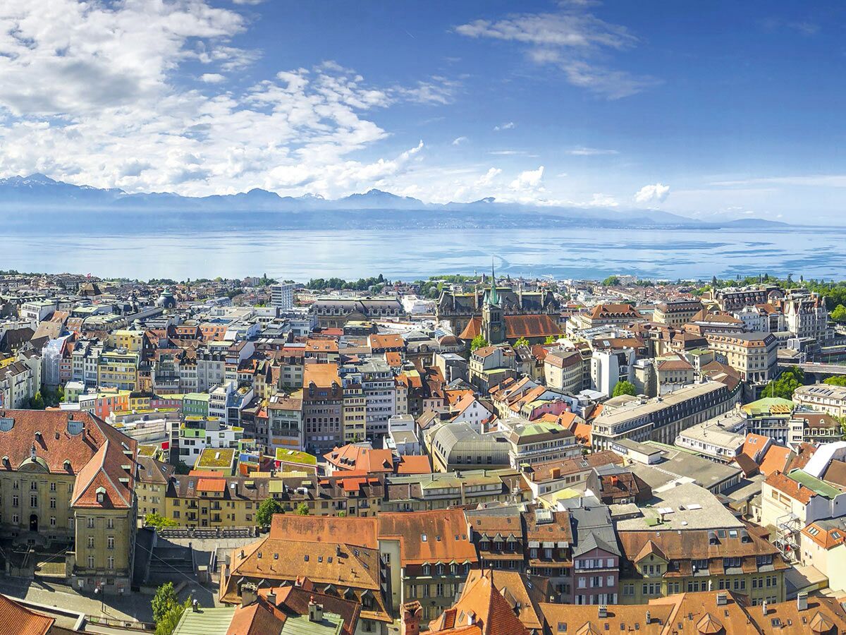 Panoramablick auf die Stadt Genf am Genfersee mit historischen Gebäuden und den Schweizer Alpen im Hintergrund.