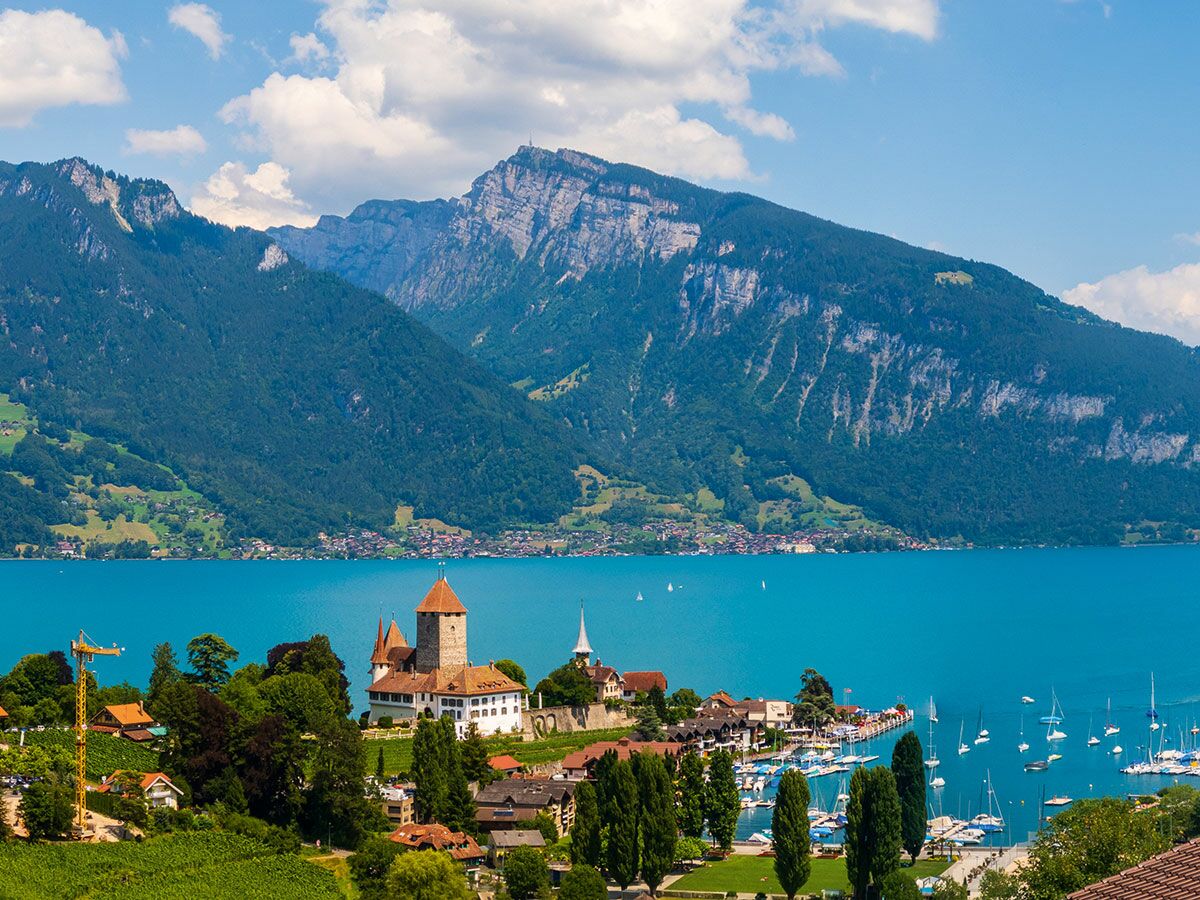 Oberhofen Schloss am Ufer des Thunersees mit Yachthafen und majestätischen Schweizer Bergen unter blauem Himmel.