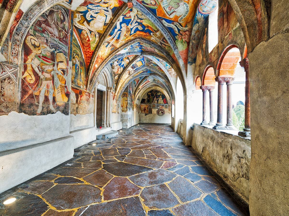 Lange gewölbte Klosterarkade mit farbenprächtigen mittelalterlichen Fresken an Wänden und Decke, mit Natursteinboden und Säulenblick.