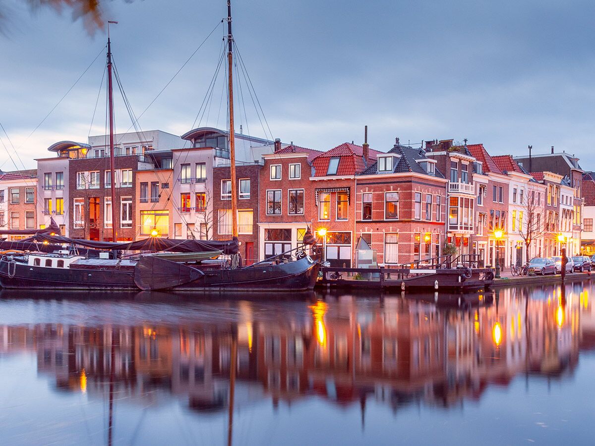 Abendliche Szene einer europäischen Kanalstadt mit historischen Häusern, modernen Gebäuden, Segelbooten und deren Reflexionen im Wasser.