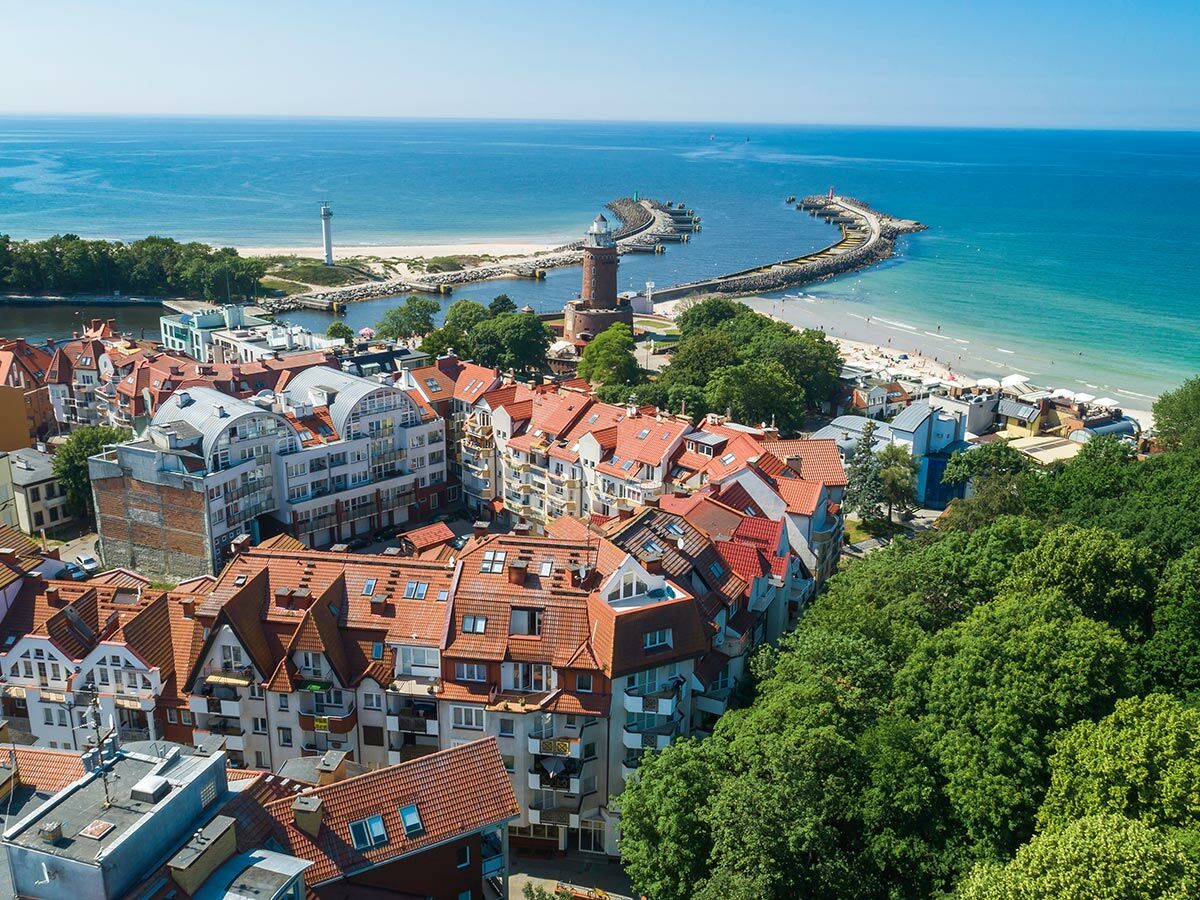 Panoramablick auf Kołobrzeg, Polen: Küstenstadt mit roten Dächern, Sandstrand, Hafenmole und Leuchttürmen an der blauen Ostsee.