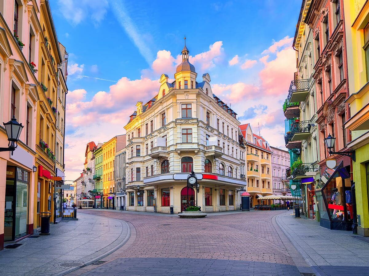 Bunte historische Gebäude in der Altstadt von Toruń, Polen, bei Sonnenaufgang mit dramatischem Himmel und leeren Straßen.