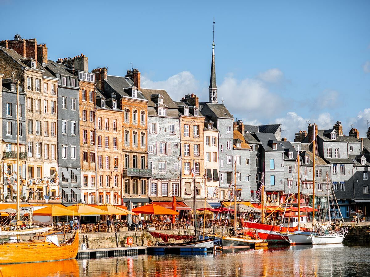 Panoramablick auf den historischen Hafen von Honfleur mit farbenfrohen Gebäuden, Restaurants und Segelbooten im Wasser.