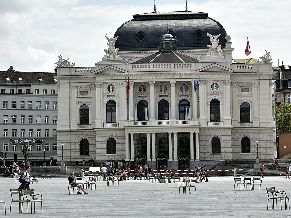 Das Opernhaus Zürich mit seiner Kuppel und klassischen Fassade am belebten Sechseläutenplatz an einem sonnigen Tag.
