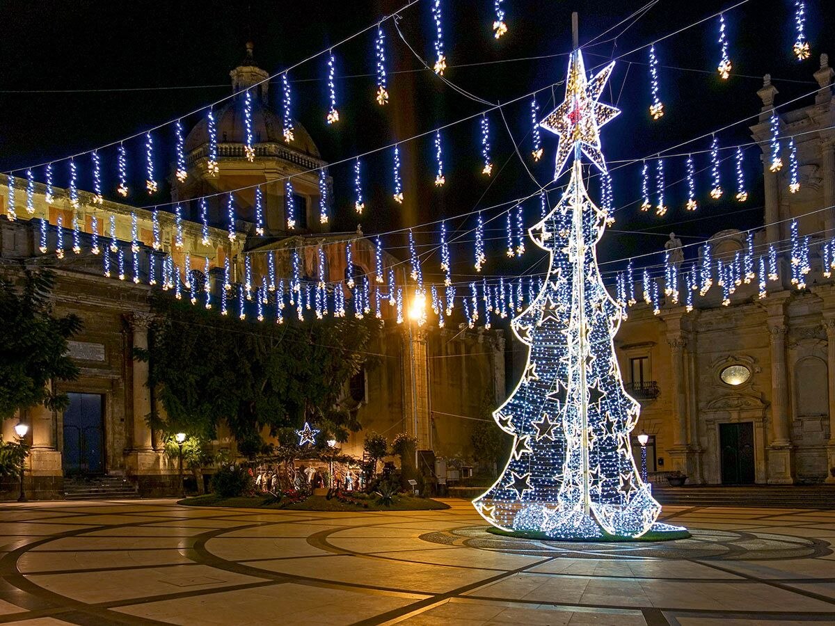 Festlich beleuchteter Stadtplatz bei Nacht mit großem leuchtendem Christbaum, Krippe und barocken Gebäuden.