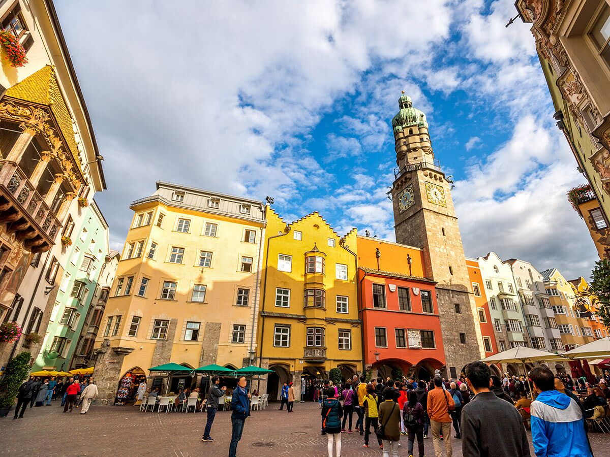 Innsbruck Altstadt mit bunten Häusern, dem Stadtturm und dem Goldenen Dachl, belebter Platz mit Touristen und Cafés.