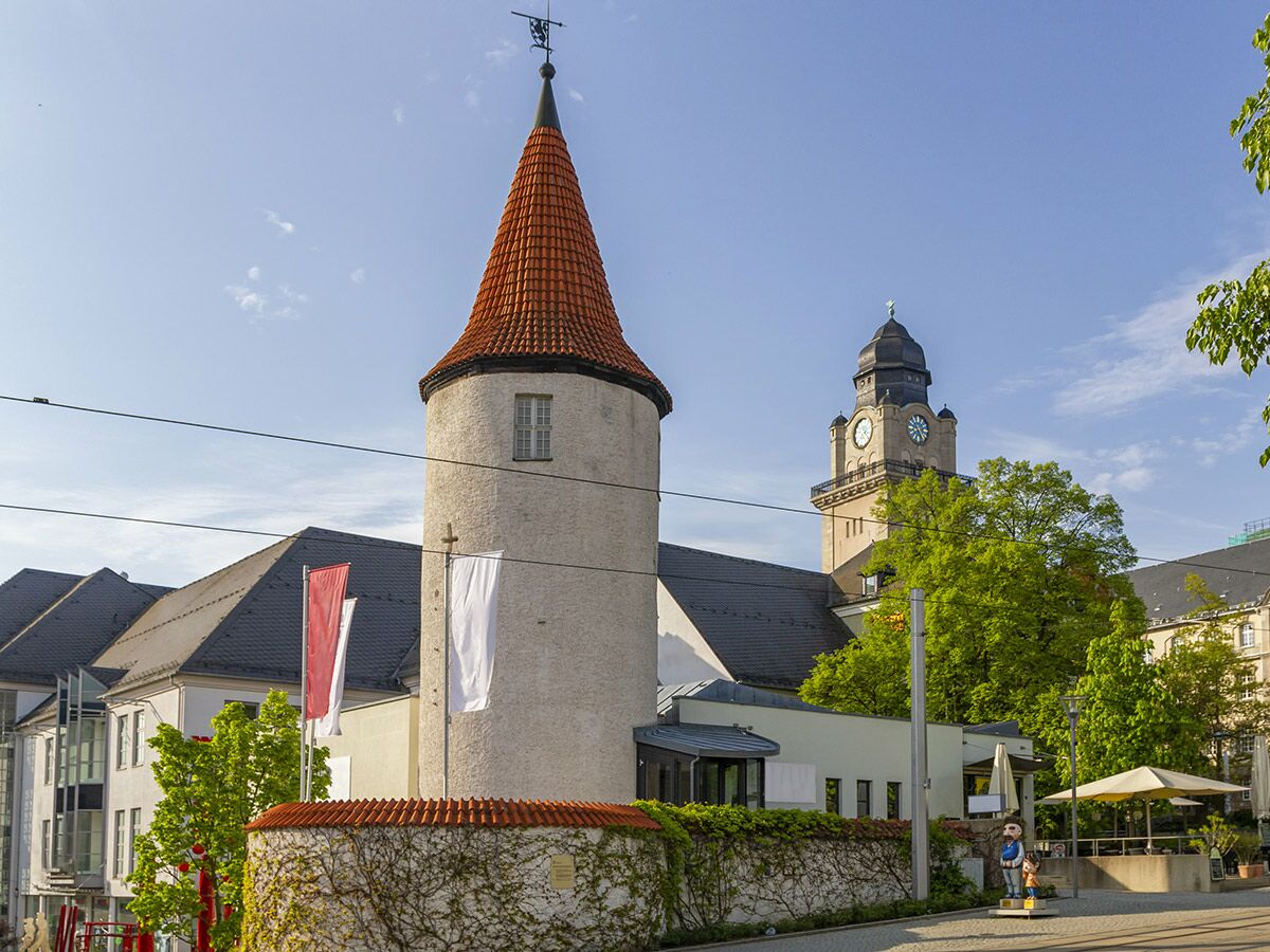 Rundturm mit rotem Dach vor dem Neuen Rathaus Leipzig. Sonniges Stadtbild mit historischen Gebäuden, Bäumen und Skulptur.