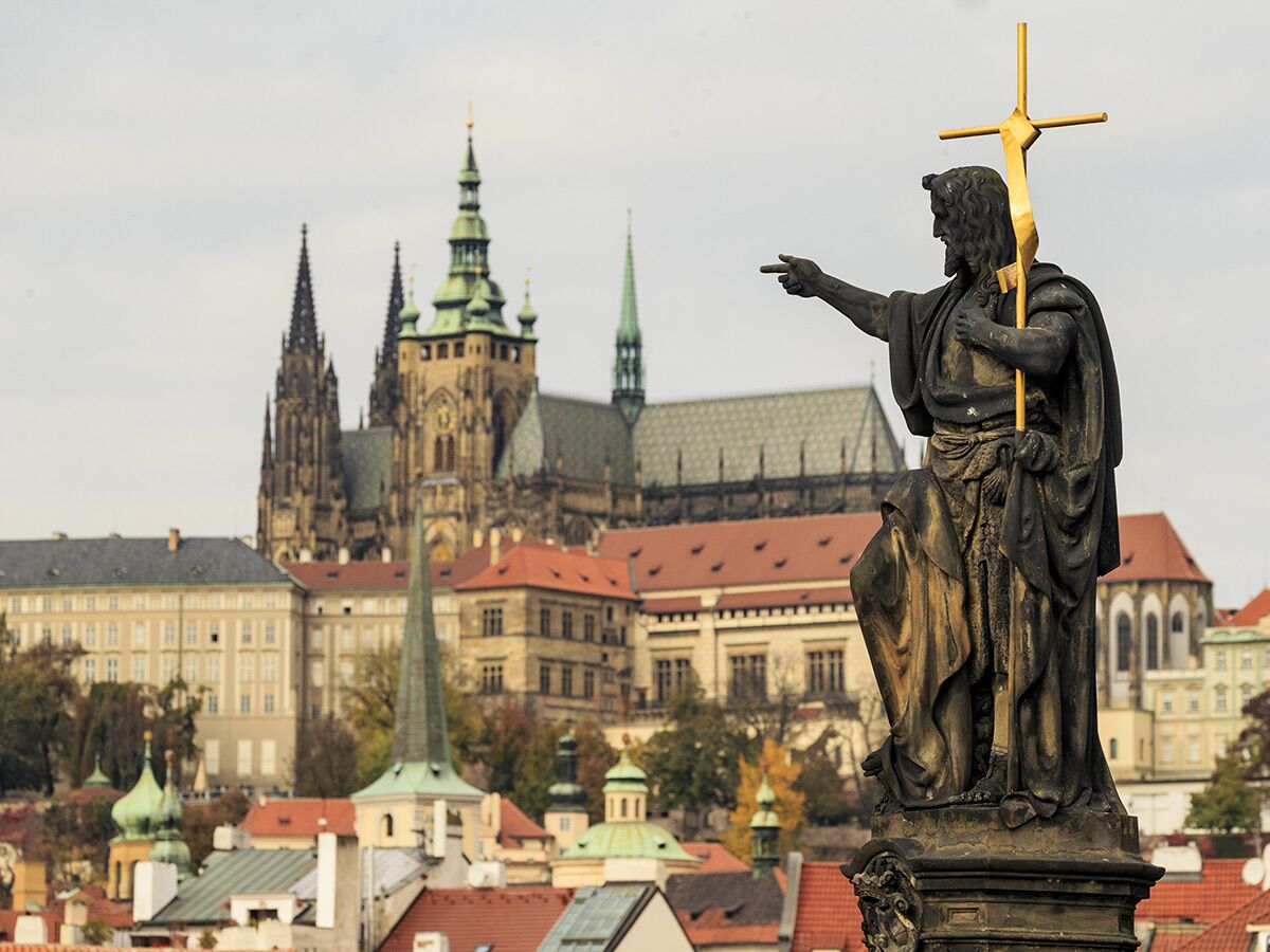 Statue des Johannes Täufers auf der Karlsbrücke zeigt auf Prager Veitsdom und Burg. Historische Stadtansicht.