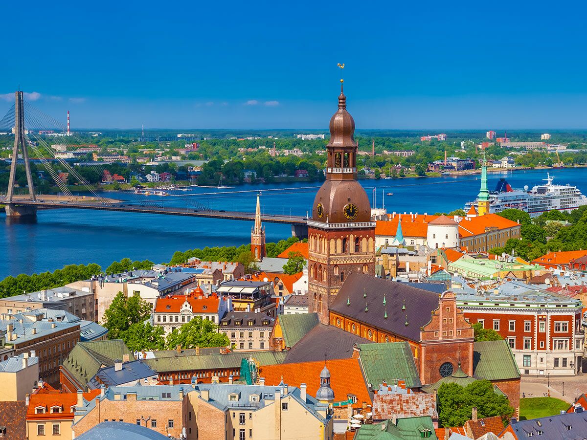 Luftaufnahme der historischen Altstadt Rigas mit Kathedrale, Daugava-Fluss, Vansu-Brücke und Kreuzfahrtschiff an einem sonnigen Tag.
