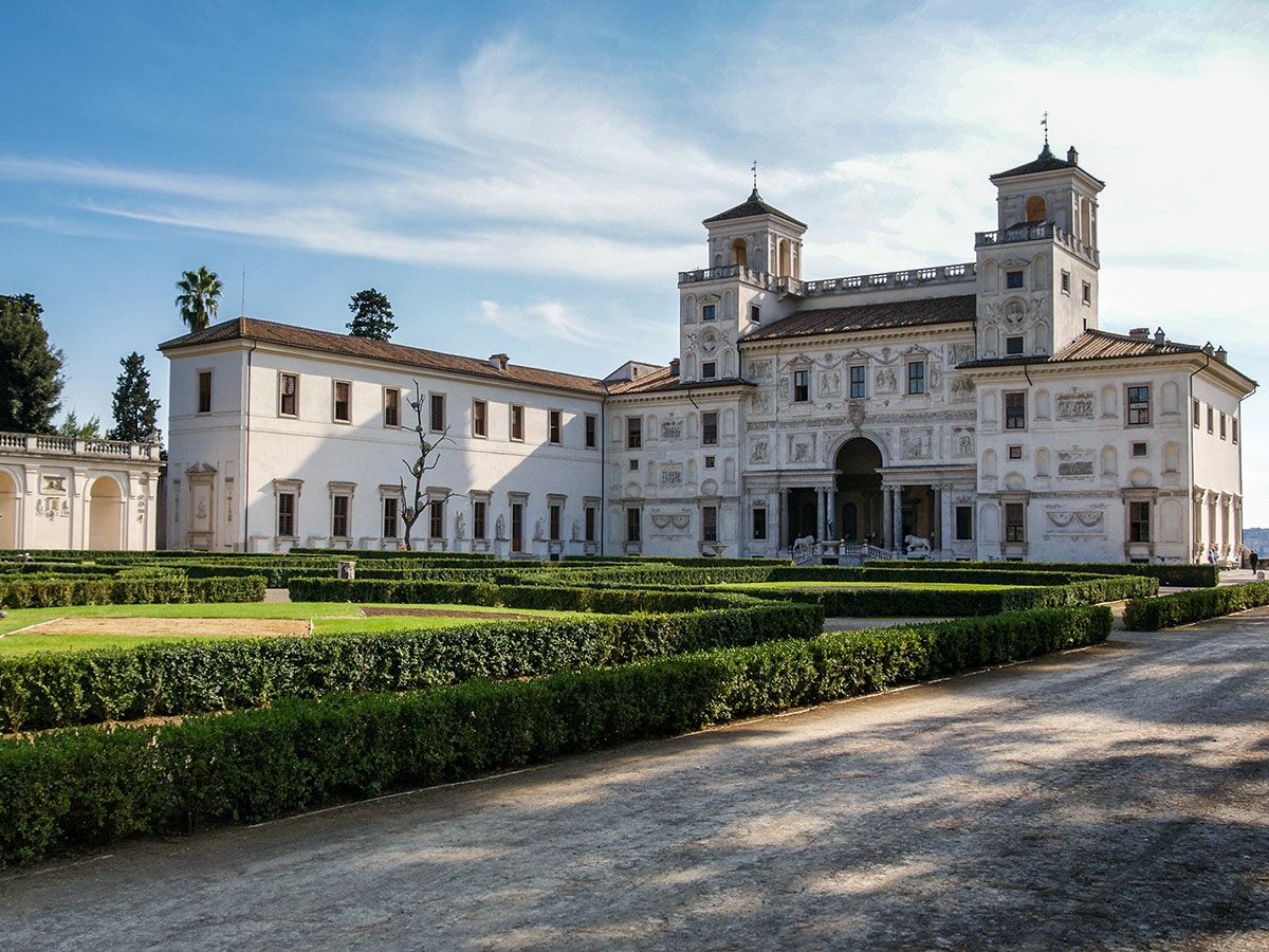 Außenansicht der prachtvollen Villa Medici in Rom mit zwei Türmen, umgeben von gepflegten Hecken und Rasenflächen.