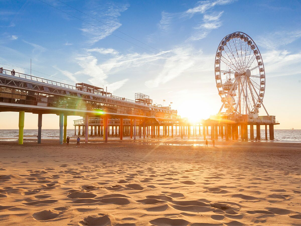 Panoramablick auf die moderne Scheveningen Pier mit Riesenrad am Sandstrand bei goldenem Sonnenuntergang.