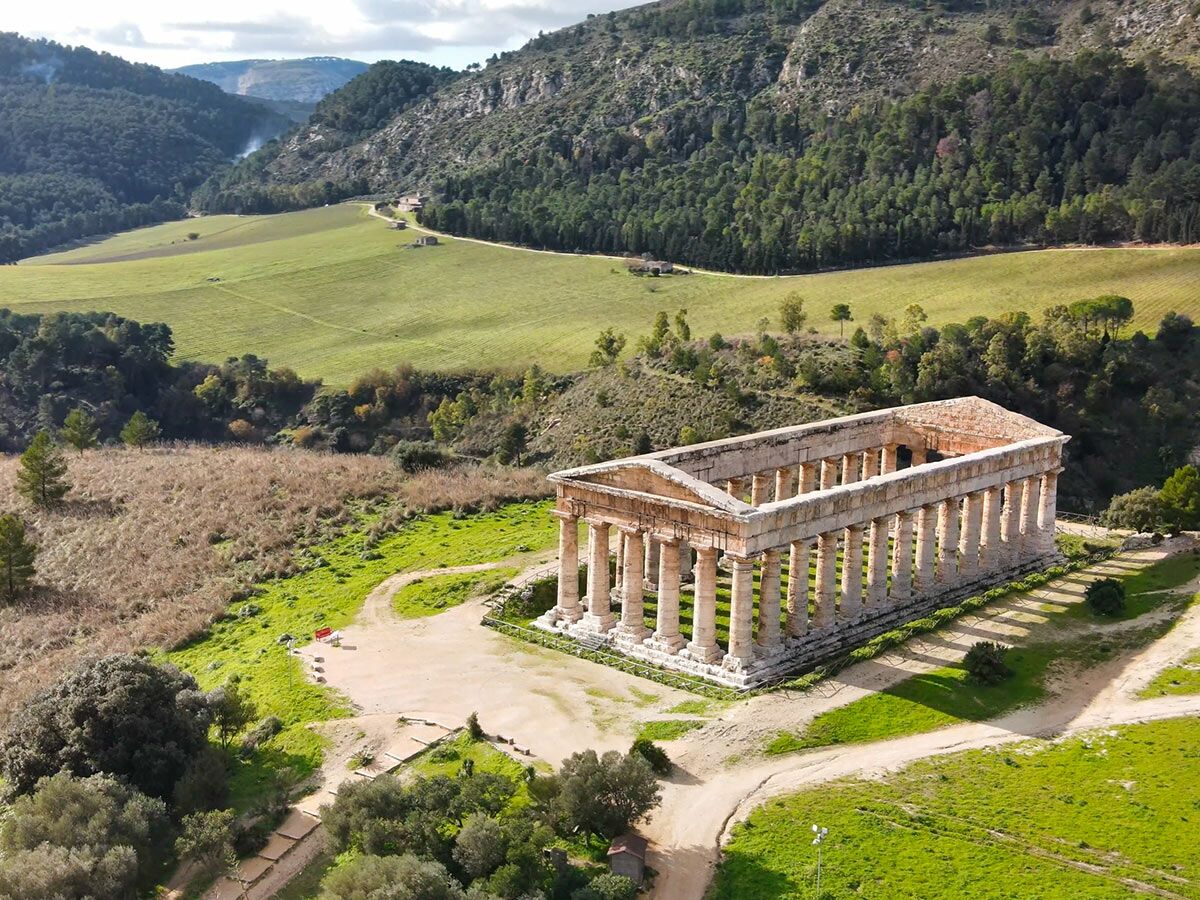 Antiker dorischer Tempel von Segesta in Sizilien, Italien, umgeben von grünen Hügeln, Feldern und Wald unter klarem Himmel.