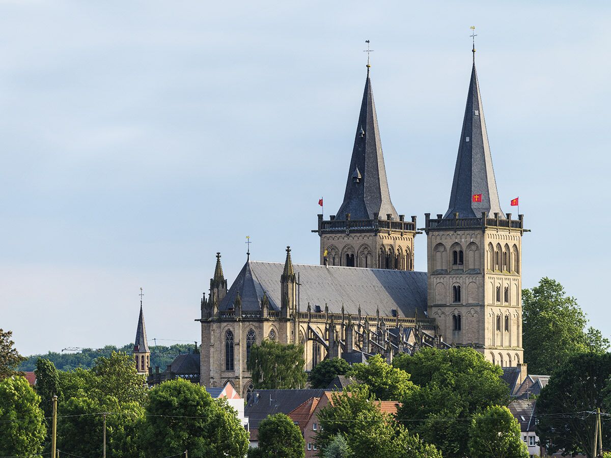 Historische St. Viktor Kathedrale in Xanten mit markanten Doppeltürmen und grünen Bäumen unter klarem Himmel.
