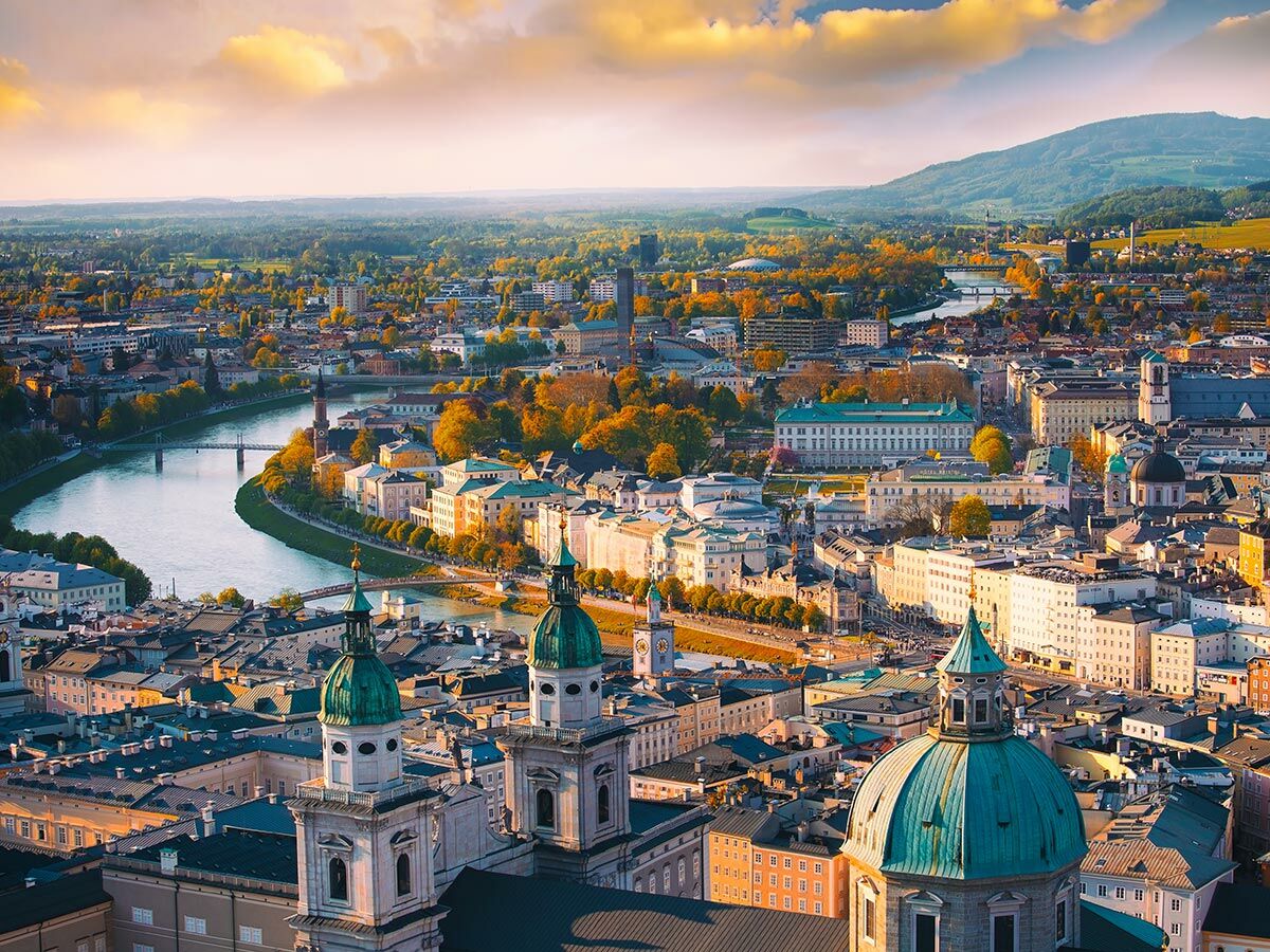 Panoramablick auf Salzburg im Herbst mit der Salzach, historischen Gebäuden, Kirchenkuppeln und Bergen bei Sonnenuntergang.