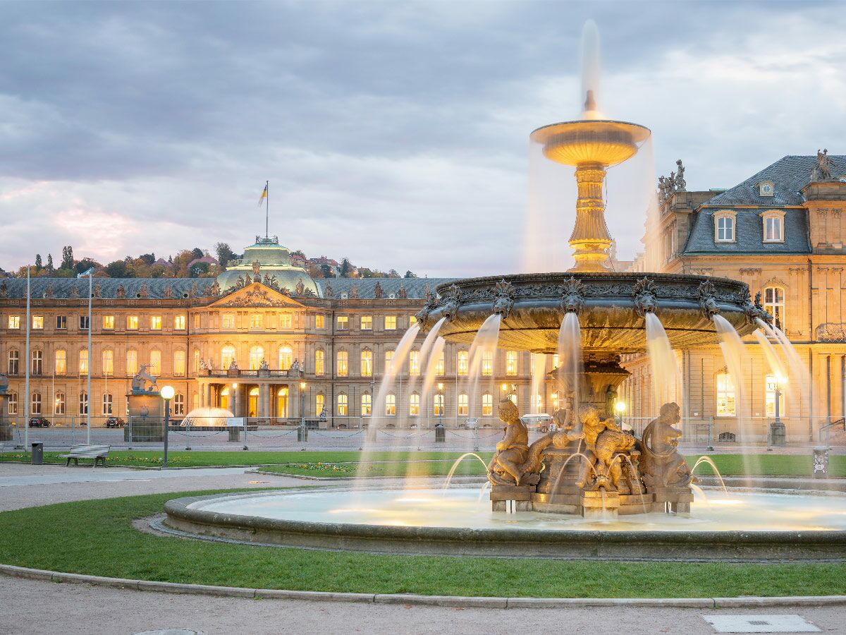 Abendansicht des beleuchteten Schlossplatzbrunnens mit dem Neuen Schloss in Stuttgart bei Dämmerung.