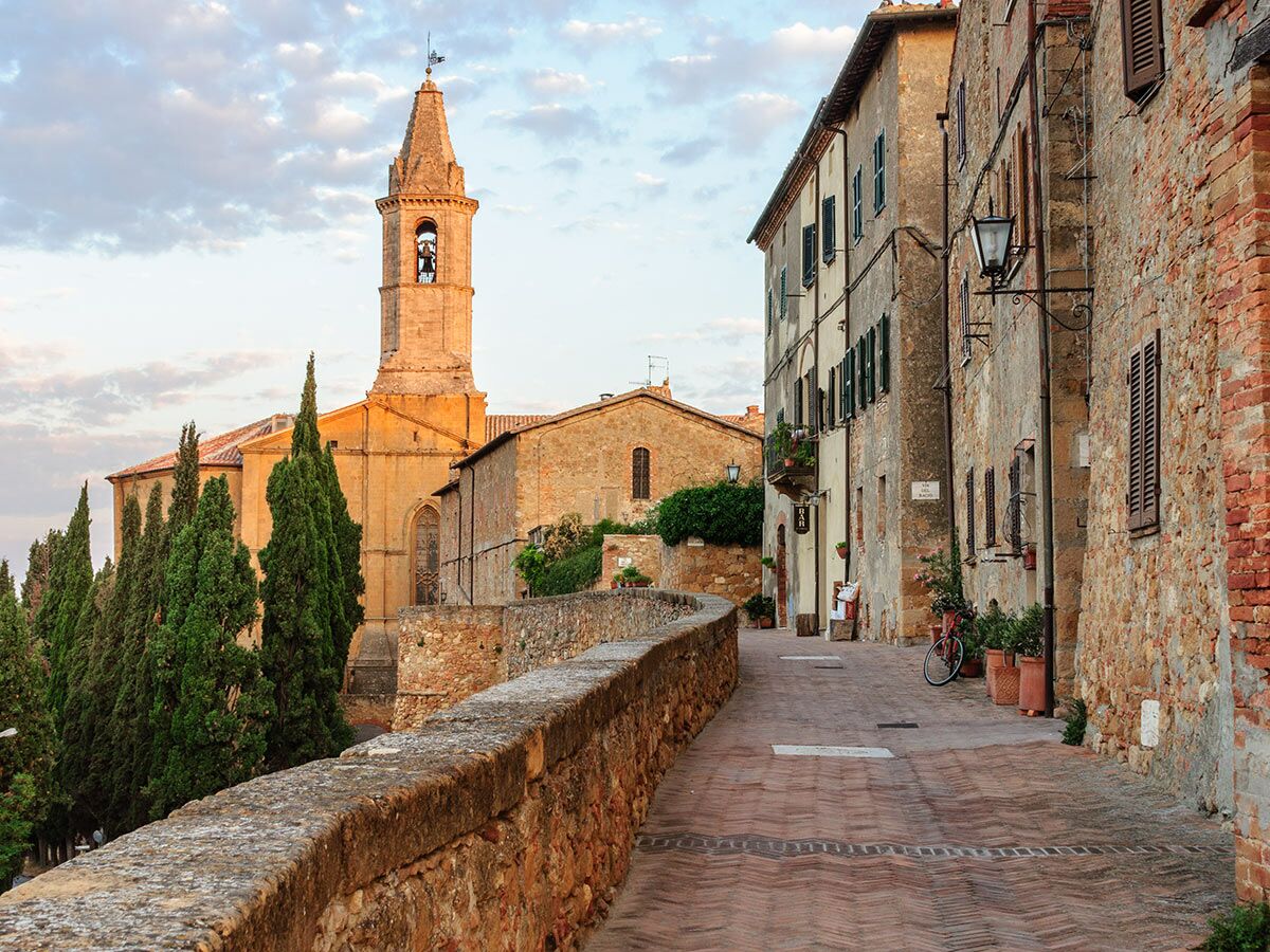 Malerische Gasse in toskanischem Dorf mit Steinhäusern, Glockenturm, Zypressen bei warmem Licht. Italienische Altstadtidylle.