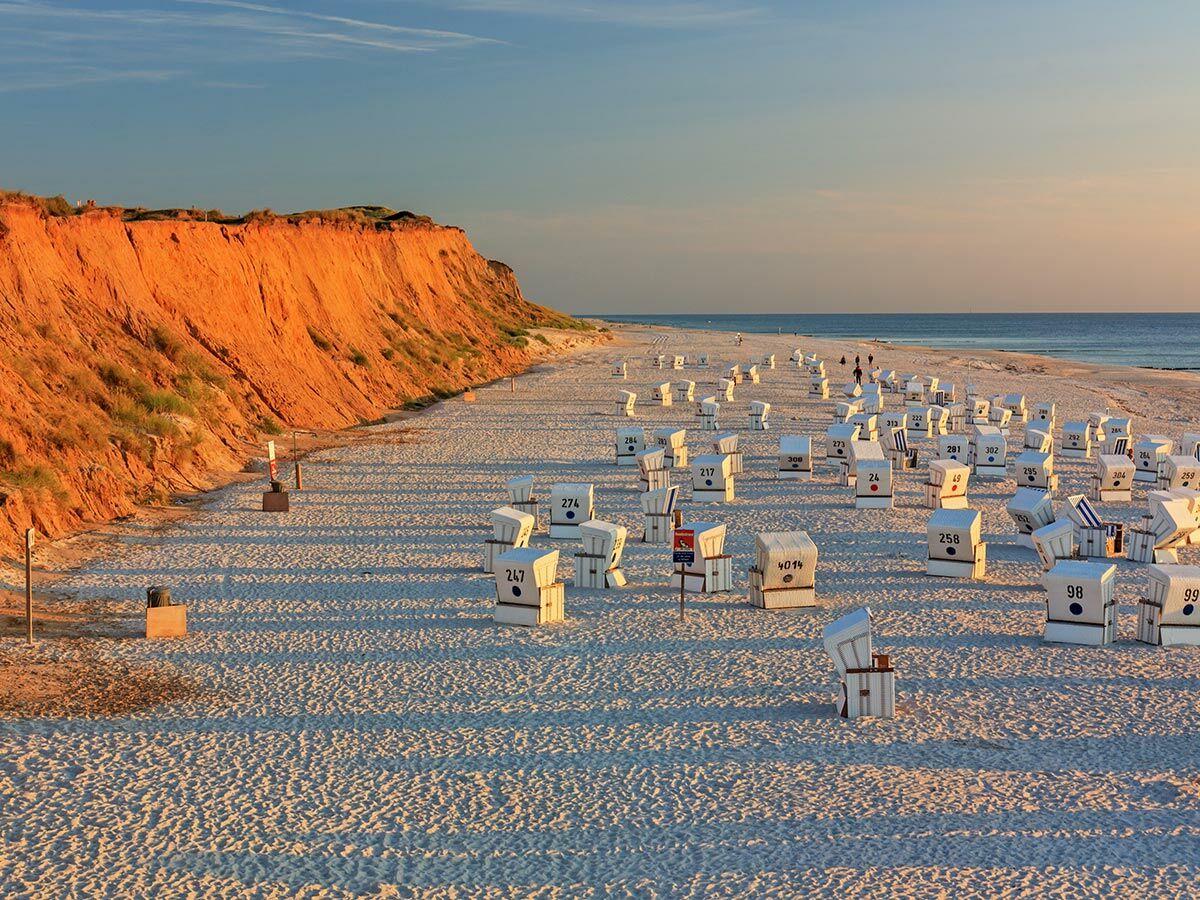 Abendstimmung am Strand von Sylt mit zahlreichen Strandkörben und dem berühmten Roten Kliff bei Sonnenuntergang.