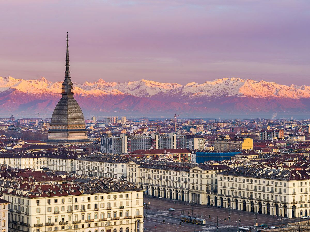 Panorama von Turin bei Sonnenuntergang mit Mole Antonelliana, historischen Gebäuden und den schneebedeckten Alpen im Hintergrund.